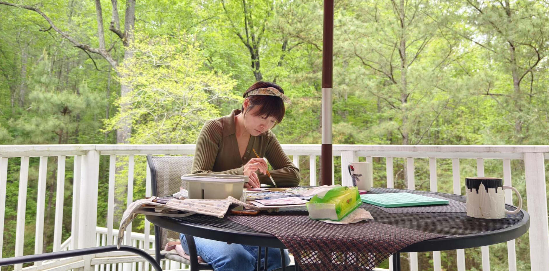Sherry at Work – Nature & Paint Artist Sherry Cheng painting watercolor outdoors on a porch, surrounded by spring greenery